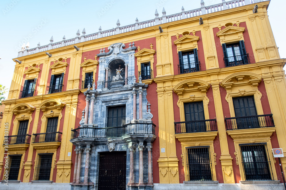 Episcopal Palace (Palacio Episcopal, Bishops Palace) on Obispo Square, Malaga, Andalusia, Spain with colorful yellow and red Spanish Baroque facade and religious art exhibitions.
