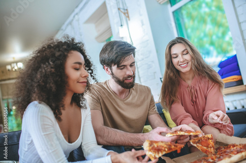 Guy and two girls taking pizza from box.