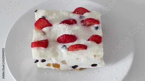 The girl adds a leaf of mint and strawberries to the dessert jelly. She sprinkles the dessert with icing sugar. It consists of berries and fruits