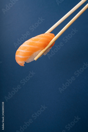 Eating fresh salmon sushi with chopstick over blue background.