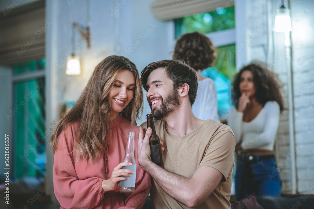 Obraz premium Guy and girl with bottles talking, two girlfriends at distance