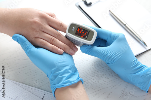 Foto Doctor examining patient with fingertip pulse oximeter at white wooden table, cl