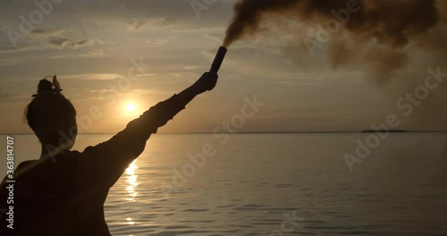 Girl on Seashore lit Signal Fire. Smoke bomb. Signal. Smoke. Pyrotechnics. Beach. Sunset. Sunset over Horizon. Gesture. Symbol. Symbolism. New Beginning. Resistance. Lighthouse. Heading. Pungent Smoke