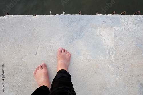 Female barefoot standing on hard cement pathway with dark river below, for a suicide concept 