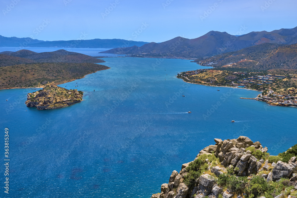 Obraz premium View of harbor between Spinalonga island and peninsula, known as Kalydon, and Plaka village from above and rocky slope in foreground, Crete, Greece.