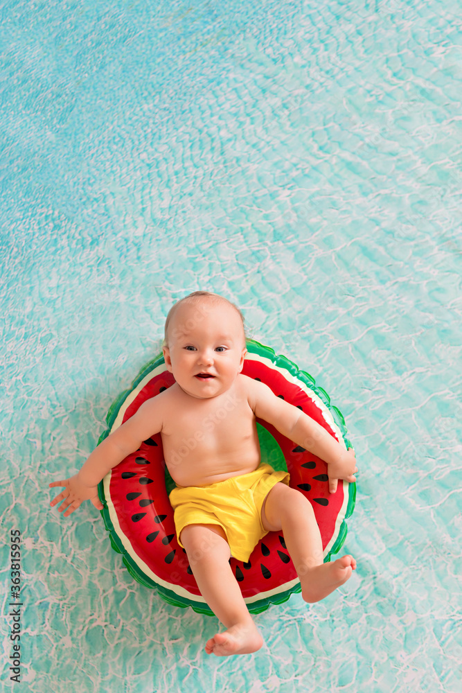 Happy little boy sunbathes on a sandy beach with palm trees by the sea. A child swims in a lifebuoy in the form of a watermelon Happy little boy sunbathes on a sandy beach with palm trees by the sea. A child swims in a lifebuoy in the form of a watermelon