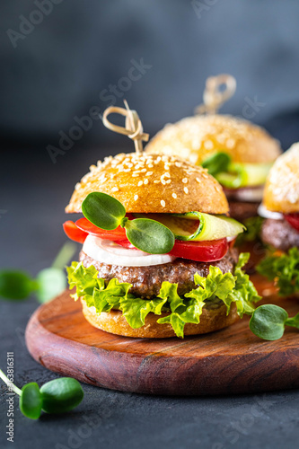 Burgers with meat cutlet, fresh lettuce, tomatoes, onions on a dark stone. copy space