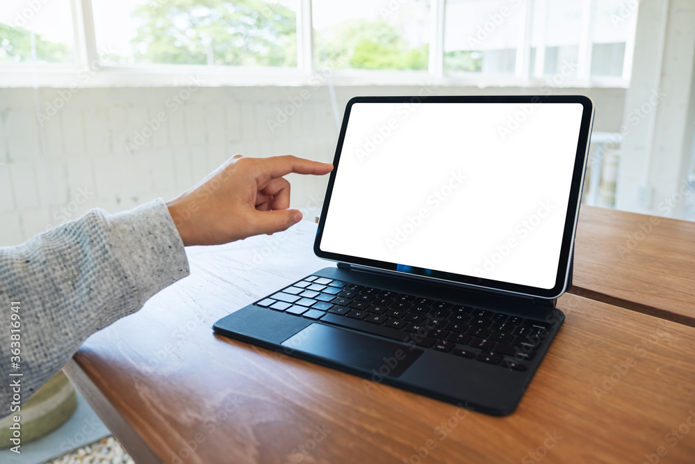 Mockup image of a woman using and pointing finger at tablet pc with blank desktop white screen as a computer pc on wooden table Mockup image of a woman using and pointing finger at tablet pc with blank desktop white screen as a computer pc on wooden table