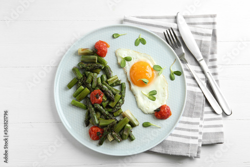 Oven baked asparagus served with fried egg on white wooden table, flat lay