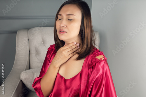 Sore throat pain symptoms. Throat infection. A woman wearing a satin nightgown and red robe suffering from hoarseness or laryngitis in the living room at night. photo