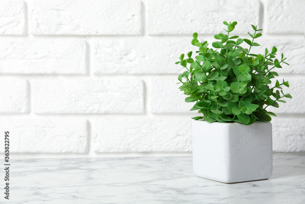 Beautiful artificial plant in flower pot on white marble table near brick wall. Space for text Beautiful artificial plant in flower pot on white marble table near brick wall. Space for text