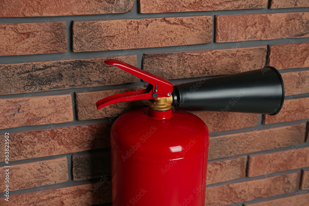 Naklejka premium Fire extinguisher near brick wall, closeup view