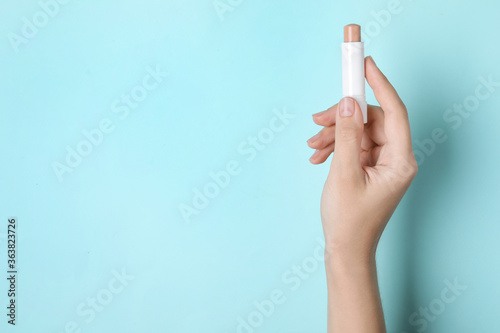 Woman holding hygienic lipstick on turquoise background, closeup. Space for text