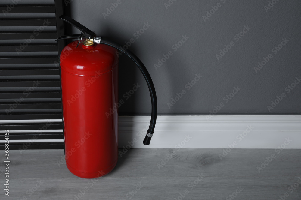 Fire extinguisher near grey wall indoors. Space for text Fire extinguisher near grey wall indoors. Space for text