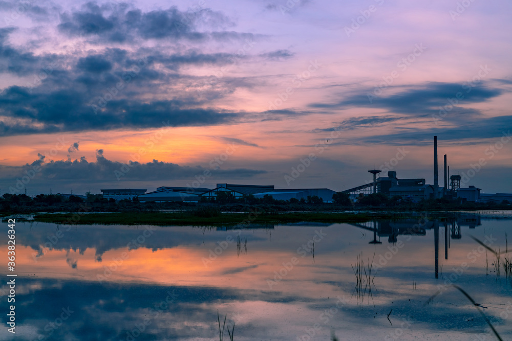 Landscape of factory industry buildings with dark blue and orange sunset sky reflection on water in the river. Warehouse building at night. Clean environment around factory. Factory closed.