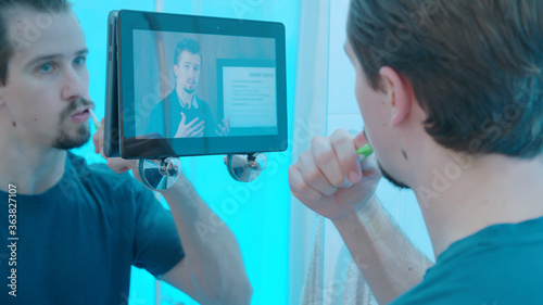 Person watching educational webinar on tablet computer while brushing teeth