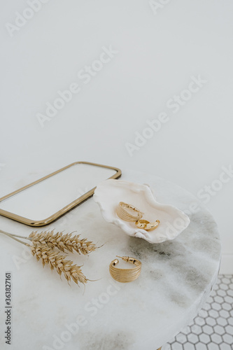 Minimal fashion composition with golden earrings in seashell on marble table with mirror and wheat stalks. Bijouterie / jewelry concept.