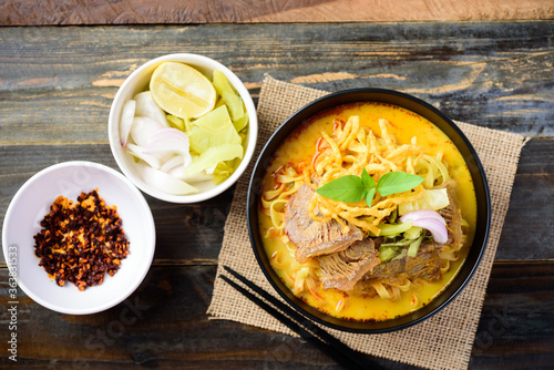 Northern Thai food (Khao Soi), Spicy curry noodles soup with beef in a bowl on wooden background