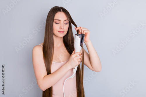 Photo of beautiful model lady long hairstyle hold electric styler curler making straight curls wavy watch result wear beige singlet isolated grey color background