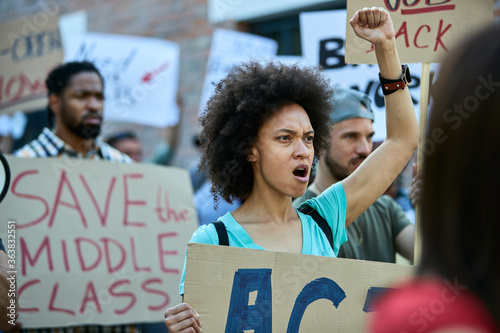 Young black woman with raised fist shouting on a protest for human rights.