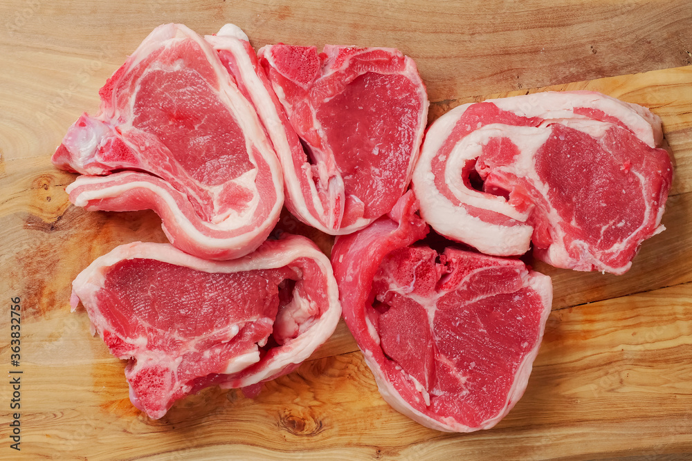 Five raw lamb chops on a wooden cutting board. Meat industry product. Top view