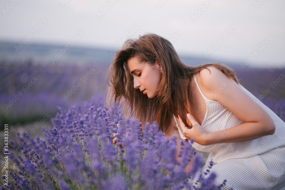 Young beautiful woman wearing straw hat and white dress relaxing in lavender field.