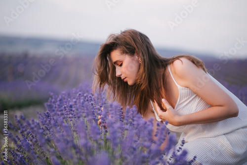 Young beautiful woman wearing straw hat and white dress relaxing in lavender field.