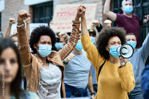 Black female activists holding hands while protesting with crowd of people during coronavirus pandemic. photo