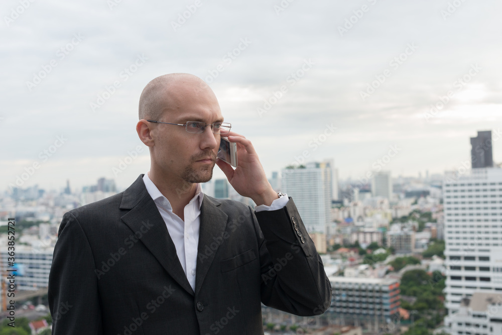 Handsome bald businessman talking on the phone against view of the city Handsome bald businessman talking on the phone against view of the city