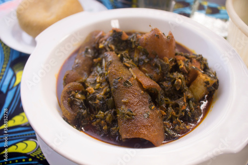 A white bowl of tasty Nigerian vegetable soup cooked with assorted meat, dried fish, cow skin (ponmo or kpomo or pomo) and Garri or Eba. Served on a colorful blue African pattern table cloth photo
