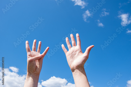 Close-up of female hands showing nine fingers on a blue sky background. Number nine in sign language. Copy space