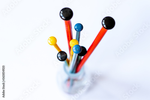 Colourful knitting needles (red, green, yellow, blue) in detail in a glass vase as seen from on top