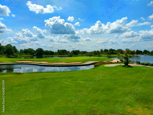 Green golf field with sand and water under cloudy blue sky photo