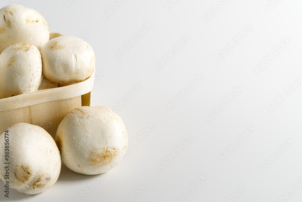 White Mushrooms champignons in wooden basket on a light background. Close up with copy space. Packed champignons to basket.