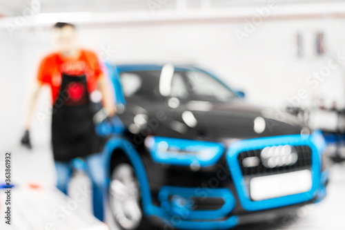 Fototapeta Naklejka Na Ścianę i Meble -  Blurred abstract image of man worker with car in body shop. Blur car auto service. Car bokeh. Blurred background with car in garage. Vehicle maintenance in auto repair service. Blurry service station