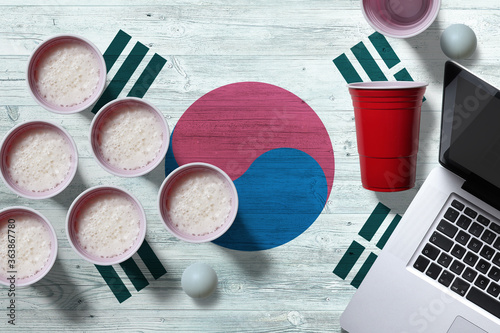 South Korea flag concept with plastic beer pong cups and laptop on national wooden table, top view. Beer Pong game.