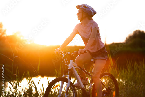 Nature. Joyful young woman riding a bicycle at the riverside and meadow promenade. Inspired by surrounded nature, summertime mood. Warm sunshine colors. Sport, activity, wellness, enjoyment concept.