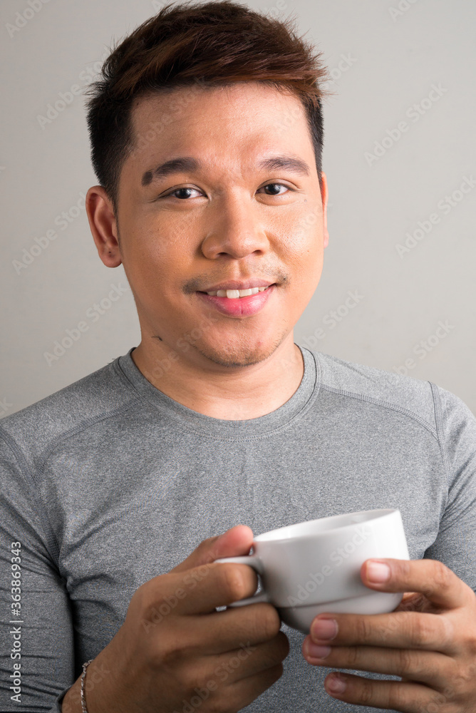 Face of happy young handsome Asian man holding coffee cup