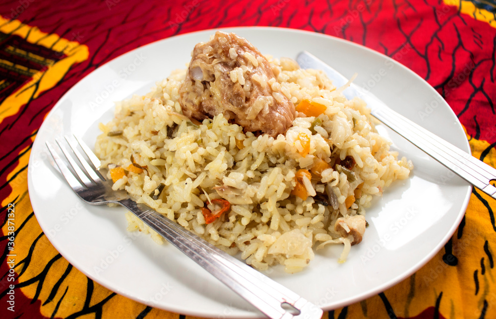 A tasty white plate of Nigerian fried rice containing sliced carrots, green beans and peppers with a piece of turkey meat on top. A fork and knife is placed on the side with a colorful red table cloth A tasty white plate of Nigerian fried rice containing sliced carrots, green beans and peppers with a piece of turkey meat on top. A fork and knife is placed on the side with a colorful red table cloth