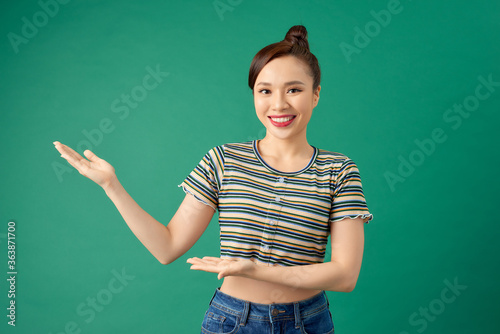 Portrait attractive young Asian woman holding copyspace on the palm isolated on green background. © makistock