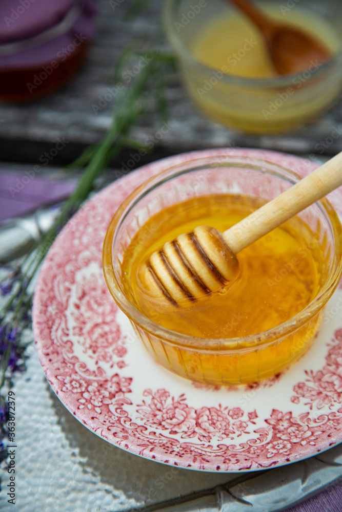 Fototapeta premium Two glass bowls with fresh natural lavender honey, jars with honey and lavender flowers on wooden background.