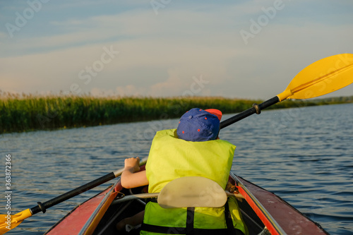 A little boy kayaks on the river in the summer and rowing an oar.