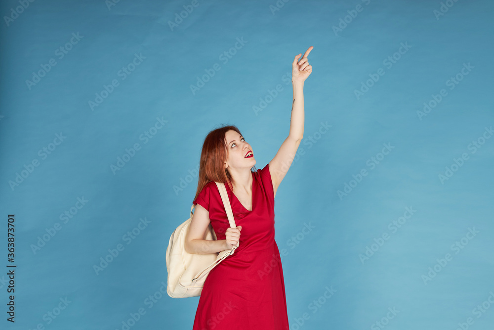 Fototapeta premium Smiling redhead girl on blue background red dress
