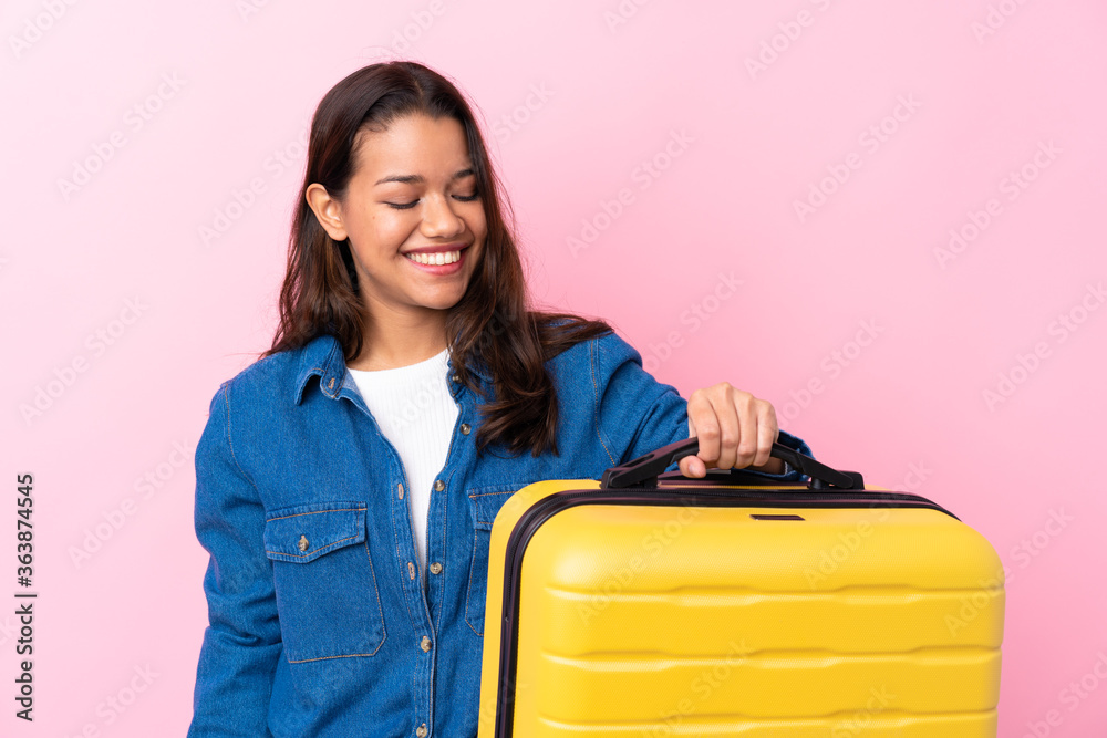 Traveler Colombian woman holding a suitcase over isolated pink background with happy expression Traveler Colombian woman holding a suitcase over isolated pink background with happy expression