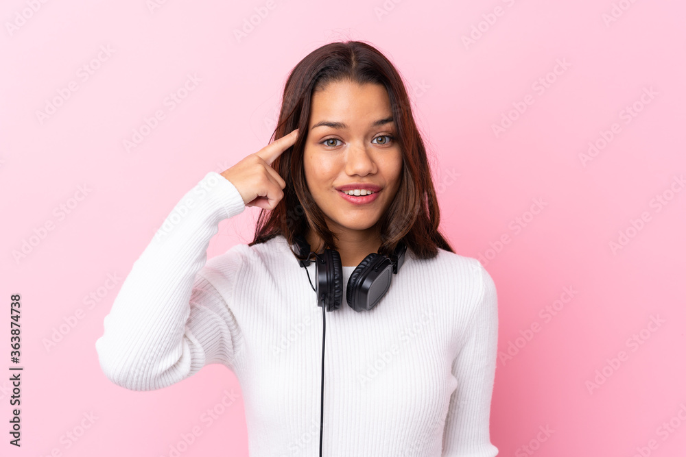 Young woman with earphones over isolated pink wall intending to realizes the solution Young woman with earphones over isolated pink wall intending to realizes the solution