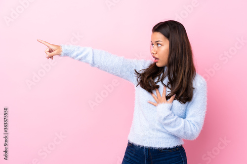 Young Colombian girl over isolated pink background pointing finger to the side