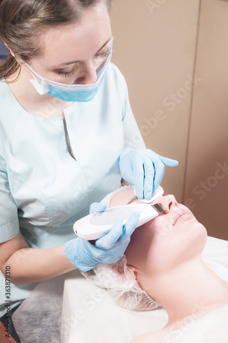 Cosmetics and facial care. Attractive girl at the reception of a beautician in the salon of beauty makes cleaning and peeling of the face with ultrasound. Beautiful and healthy facial skin