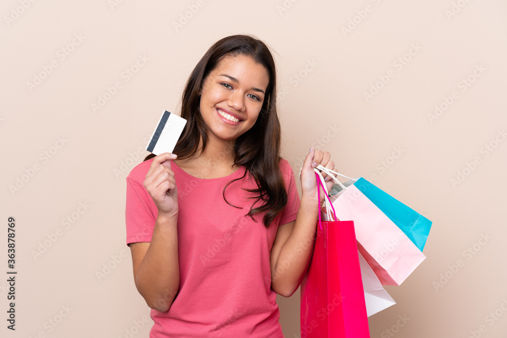 Young Colombian girl with shopping bag over isolated background holding shopping bags and a credit card Young Colombian girl with shopping bag over isolated background holding shopping bags and a credit card