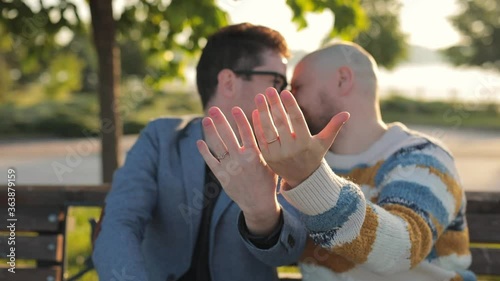 Gay Marriage Proposal Concept. Adorable Boyfriend kissing and show his Beautiful Shiny Wedding Rings to camera. Surprised Partner is Extremelly Happy and Hugs His Queer Friend. Relationship Goals. photo