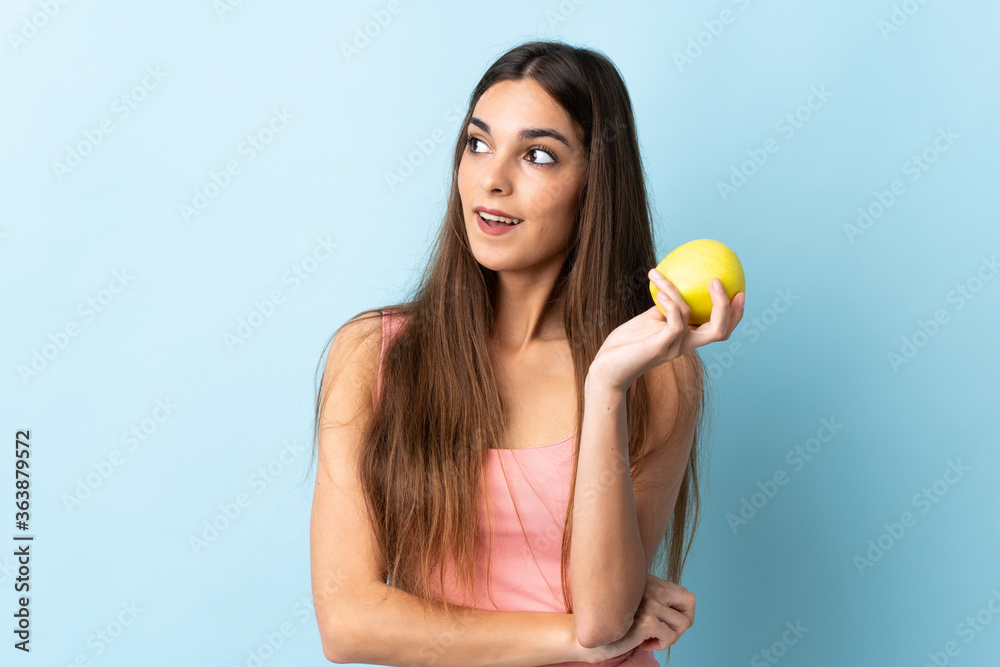 Young caucasian woman isolated on blue background with an apple and happy Young caucasian woman isolated on blue background with an apple and happy